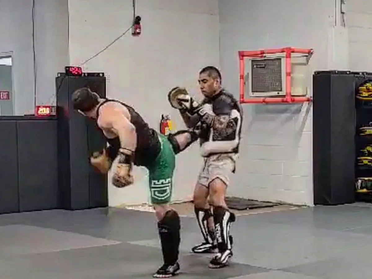 A member landing a Muay Thai kick on the coach's Thai pads at Furst Place MMA